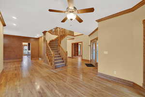 Unfurnished living room with stairway, ornamental molding, french doors, light wood-style floors, and a ceiling fan