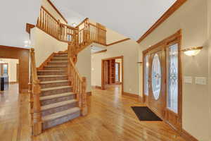 Entryway with ornamental molding, stairway, light wood-style flooring, and a high ceiling