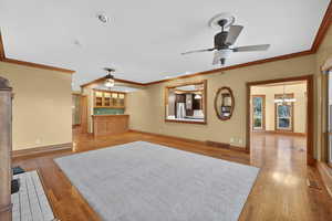 Unfurnished living room with a ceiling fan, light wood-type flooring, crown molding, and a chandelier