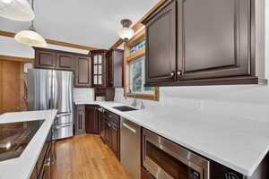 Kitchen featuring stainless steel appliances, dark brown cabinets, light wood-style floors, light stone counters, and pendant lighting