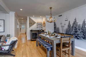 Dining room with beverage cooler, light wood-style floors, ornamental molding, bar with sink, and a chandelier