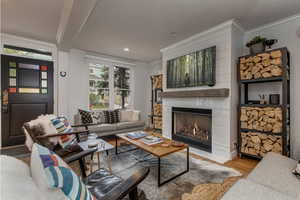 Living room with ornamental molding, a warm lit fireplace, light wood-style flooring, recessed lighting, and beamed ceiling