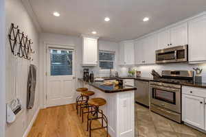 Kitchen featuring stainless steel appliances, white cabinets, a kitchen breakfast bar, dark stone countertops, and recessed lighting