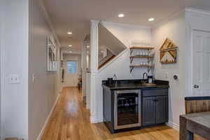 Indoor wet bar with ornate columns, beverage cooler, open shelves, light wood-style floors, and recessed lighting