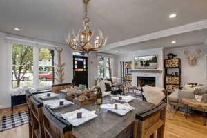 Dining room with a fireplace, light wood finished floors, crown molding, and hanging lights
