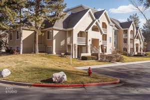 View of front facade with roof with shingles, uncovered parking, a front lawn, and a balcony