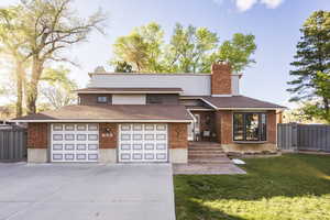 View of front facade with driveway, a chimney, a shingled roof, and brick siding