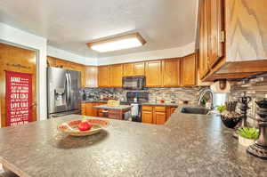 Kitchen featuring black appliances, wood finish cabinetry, backsplash, a textured ceiling, and dark countertops