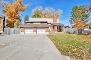 View of front facade featuring brick siding, concrete driveway, a chimney, a gate, and roof with shingles