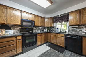Kitchen with black appliances, wood finish cabinets, dark wood-style floors, and dark stone countertops