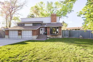 View of front facade featuring driveway, a chimney, brick siding, and an attached garage