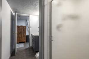 Full bathroom with a shower stall, vanity, a textured ceiling, and dark wood-style flooring