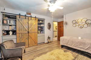 Bedroom featuring a barn door, wood finished floors, a textured ceiling, and ceiling fan