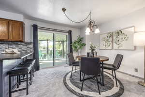 Dining room featuring light carpet, hanging lights, and a textured ceiling