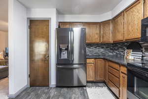 Kitchen with black appliances, wood finish cabinetry, dark wood-style floors, and backsplash