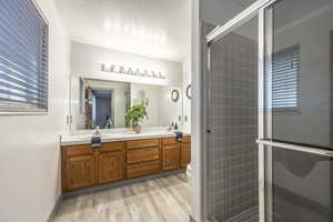 Bathroom featuring double vanity, light wood-style flooring, a stall shower, and a textured ceiling