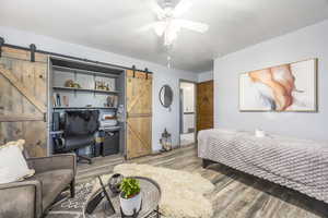 Bedroom with a barn door, wood finished floors, a textured ceiling, a desk, and a ceiling fan