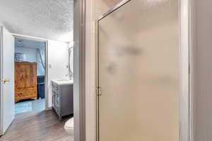 Full bathroom featuring a textured ceiling, vanity, a shower stall, and dark wood-type flooring