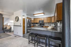 Kitchen featuring a kitchen breakfast bar, dark countertops, wood finish cabinets, black appliances, and a peninsula