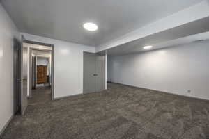 Finished basement with dark colored carpet and a textured ceiling