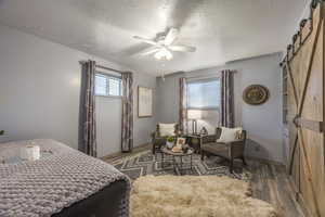 Bedroom with a barn door, a textured ceiling, multiple windows, wood finished floors, and a ceiling fan