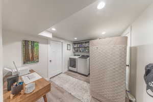 Laundry area featuring light wood-style flooring, recessed lighting, washer and clothes dryer, and a desk