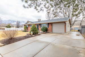 Ranch-style home with driveway, brick siding, a chimney, and an attached garage