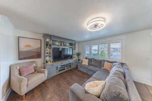 Living area with dark wood finished floors, a textured ceiling, and crown molding