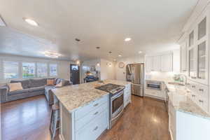 Kitchen featuring stainless steel appliances, white cabinets, hanging light fixtures, dark wood-style flooring, and open floor plan