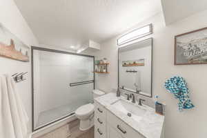 Full bathroom featuring vanity, a stall shower, light wood-style floors, and a textured ceiling