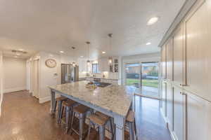Kitchen with a breakfast bar, light stone counters, a kitchen island, dark wood finished floors, and a textured ceiling