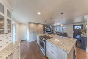 Kitchen featuring stainless steel gas stove, light stone countertops, decorative light fixtures, and open floor plan