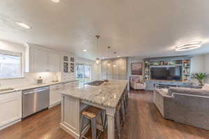 Kitchen featuring a kitchen breakfast bar, pendant lighting, dishwasher, light stone counters, and glass insert cabinets