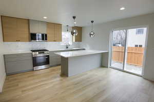 Kitchen featuring a peninsula, stainless steel appliances, pendant lighting, and light wood-style flooring