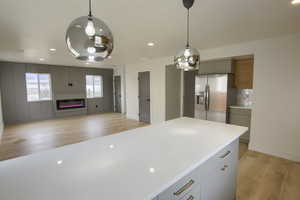 Kitchen featuring open floor plan, light wood finished floors, gray cabinetry, hanging light fixtures, and stainless steel refrigerator with ice dispenser