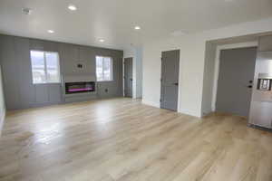 Unfurnished living room featuring light wood-style floors, a glass covered fireplace, and recessed lighting