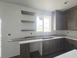 Kitchen featuring open shelves, dark wood finish cabinets, dark wood-style floors, and built in desk