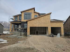 View of front of house with a garage, roof with shingles, a mountain view, and gravel driveway