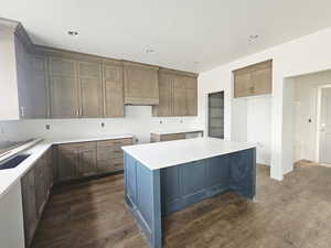 Kitchen with dark wood-style flooring, light stone counters, a center island, a kitchen bar, and two tone cabinetry
