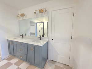 Full bath with light floors, double vanity, and a shower stall