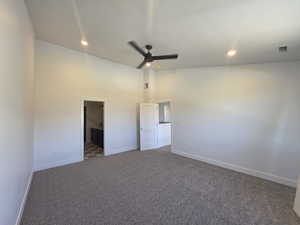 Unfurnished bedroom featuring a ceiling fan, dark carpet, ensuite bathroom, lofted ceiling, and recessed lighting