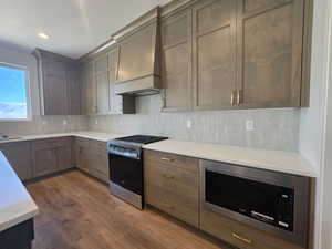 Kitchen with stainless steel appliances, backsplash, dark wood finished floors, light stone countertops, and recessed lighting