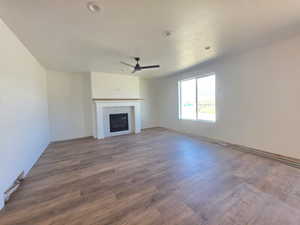 Unfurnished living room with a tile fireplace, dark wood finished floors, and a ceiling fan