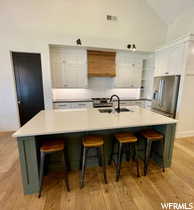 Two tone kitchen with lofted ceiling, stainless steel appliances, light wood-style floors, a breakfast bar area, and light countertops