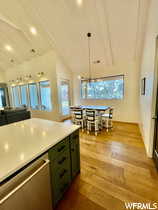 Kitchen featuring green cabinets, vaulted ceiling, stainless steel dishwasher, light wood-style floors, and pendant lighting