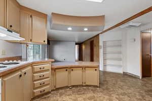 Kitchen with light countertops, built in shelves, a peninsula, stone finish floors, and white electric cooktop