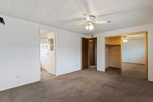 Unfurnished bedroom featuring carpet flooring, a closet, a ceiling fan, ensuite bathroom, and wooden walls