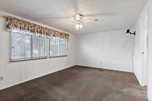 Carpeted empty room featuring a ceiling fan, a textured ceiling, and wooden walls