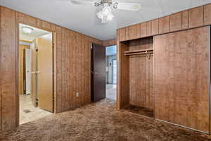 Unfurnished bedroom featuring carpet floors, ceiling fan, wood walls, and a closet