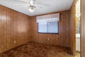 Unfurnished room with a ceiling fan, dark carpet, and wooden walls
